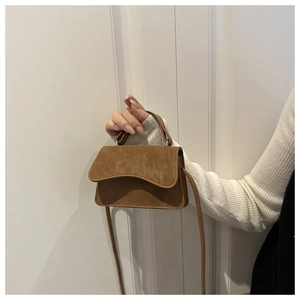 Handheld view of a brown suede mini square bag showing size scale and top handle
