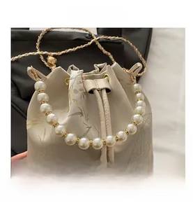 Detail view of floral embroidery on beige bucket bag with pearl handle and gold chain
