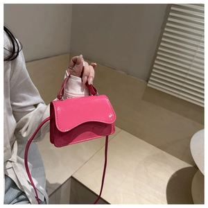 Detail of rose pink patent leather mini bag with wavy flap shown on model's hand