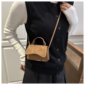 Close-up of mini brown suede handbag with wavy flap and adjustable shoulder strap