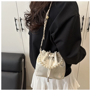Detail of cream bucket bag with floral embroidery, pearl handle and gold chain strap
