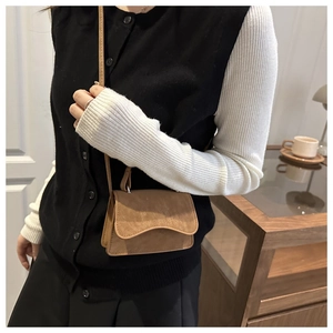 Brown faux suede crossbody bag with wave flap design worn by model in cozy interior