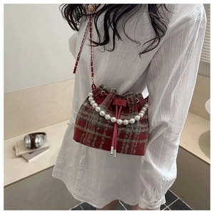 Detail of red plaid tweed bucket bag featuring pearl handle and chain strap on a model