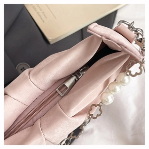 Detail of light pink pleated handbag featuring decorative pearl and floral metal chain