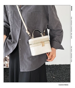 Close-up of off-white crocodile pattern handbag with golden zipper and top handle