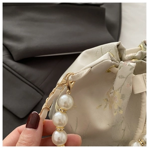 Detail of floral jacquard fabric with pearl strap and golden lobster clasp on bucket bag