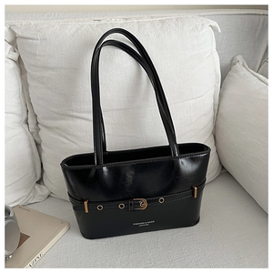 Détail du sac baguette noir en cuir ciré avec boucle métallique et sangle sur un canapé