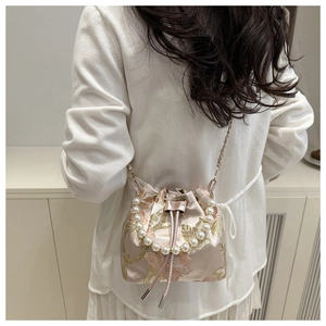 Detail of floral embroidery and pearl handle on pink satin bucket bag shown on model