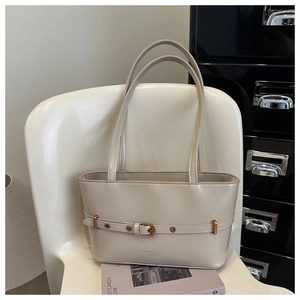 Detail shot of a beige leather shoulder bag with buckle strap on a white chair