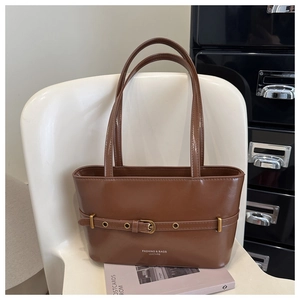 Detail of a brown leather shoulder bag with decorative belt buckle on a white chair
