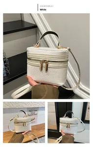 Detail of white box bag featuring crocodile texture and golden zippers with top handle