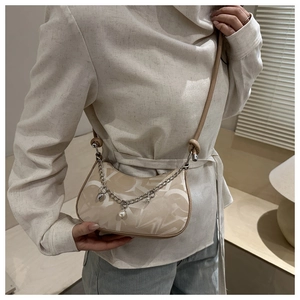 Detail of beige half-moon bag with letter patterns, silver chain, and pearl charm