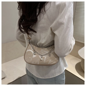 Detail view of the elegant chain strap with pearl and heart charms on a beige crescent bag