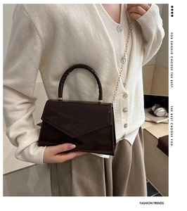 Detail of a shiny dark brown patent leather crossbody bag with a chain strap and flap