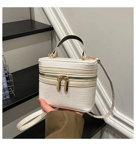 Detail of white crocodile pattern box handbag with golden metal zippers and black handle