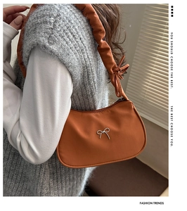 Detail of orange crescent bag featuring silver bow buckle and ruched shoulder strap