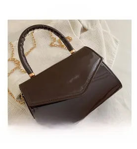 Detail of dark brown patent leather handbag with glossy finish and gold chain strap