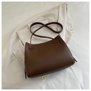 Flat lay of dark brown leather shoulder bag on a beige blazer and white sheet