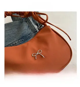 Detail of orange shoulder bag with silver butterfly buckle and gathered handle design