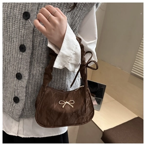 Detailed view of brown ruched handbag featuring a decorative gold metal bow accent