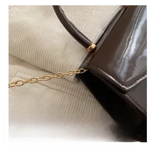 Detail of dark brown patent leather handbag with gold metal chain and smooth handle