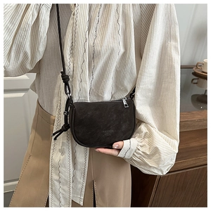 Detail of dark brown matte saddle bag featuring embossed logo and knotted shoulder strap