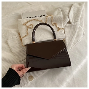 Close-up of a glossy dark brown patent leather handbag with a gold chain on velvet