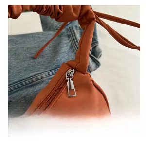 Detail view of smooth silver metal zipper on a burnt orange gathered crescent handbag