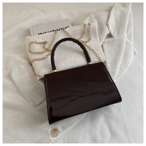 Detail of glossy brown patent leather bag with gold chain strap on soft white fabric