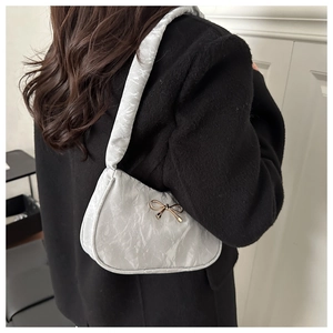 Detail view of a silver textured underarm bag with a golden bow on model shoulder