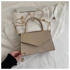 Detail of a beige patent leather handbag with a gold chain strap on a textured surface