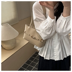 Detail of beige shoulder bag featuring decorative buckle strap and dual slender straps