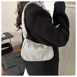 Close-up of light gray pleated underarm bag with gold metal bow on a black coat