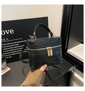 Detail of black crocodile embossed leather box bag with golden double zipper and handle