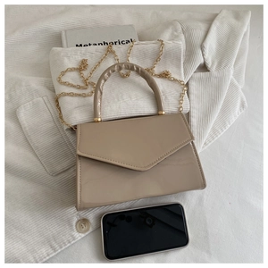 Macro detail of glossy beige patent leather bag with gold chain and thickened handle