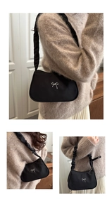 Close-up of black shoulder bag featuring silver bow detail and ruffled pleated strap