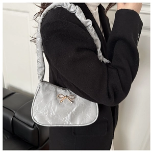 Détail du sac sous le bras plissé argenté avec un nœud doré métallique élégant