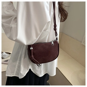 Detail of burgundy crescent crossbody bag featuring decorative knot and logo embossing