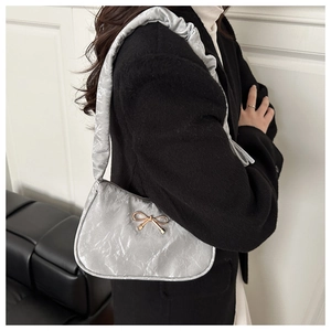 Detail of silver pleated shoulder bag featuring a metallic gold bow and soft textured fabric
