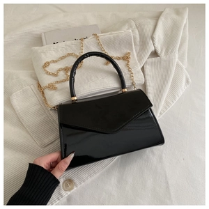 Detail of black glossy patent leather small square bag with golden chain and V-flap cover