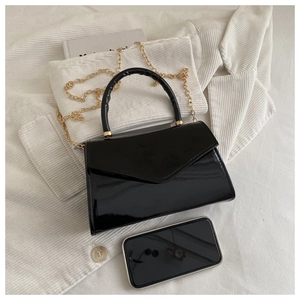 Detail of a mini glossy patent leather handbag with gold chain strap and smartphone for scale