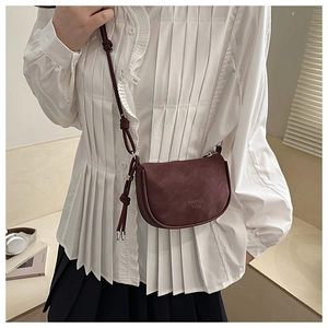 Side view of a vintage wine red half-moon leather crossbody bag on a model in white shirt