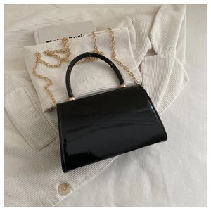 Close-up of glossy black patent leather handbag with gold chain strap and top handle