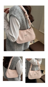 Detail view of pink underarm bag with a silver metal bow and ruched shoulder strap