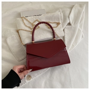 Detail of red patent leather handbag with curved handle and gold chain strap