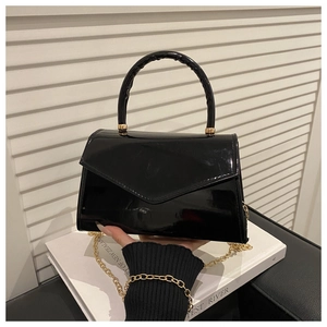 Detail of glossy black patent leather handbag with gold chain and round top handle