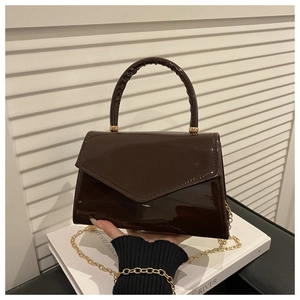 Detail of dark brown glossy patent leather handbag with gold chain strap and top handle