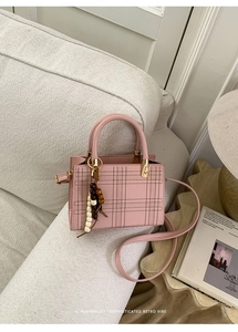 Detail of pink plaid handbag with retro bead charm on a soft tweed sofa surface