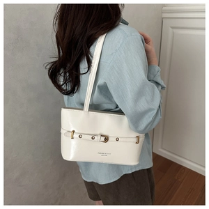 Detailed side view of white leather underarm bag with gold buckle and adjustable strap