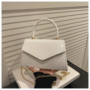 Close-up of white patent leather handbag with glossy trapezoid shell and gold chain strap
